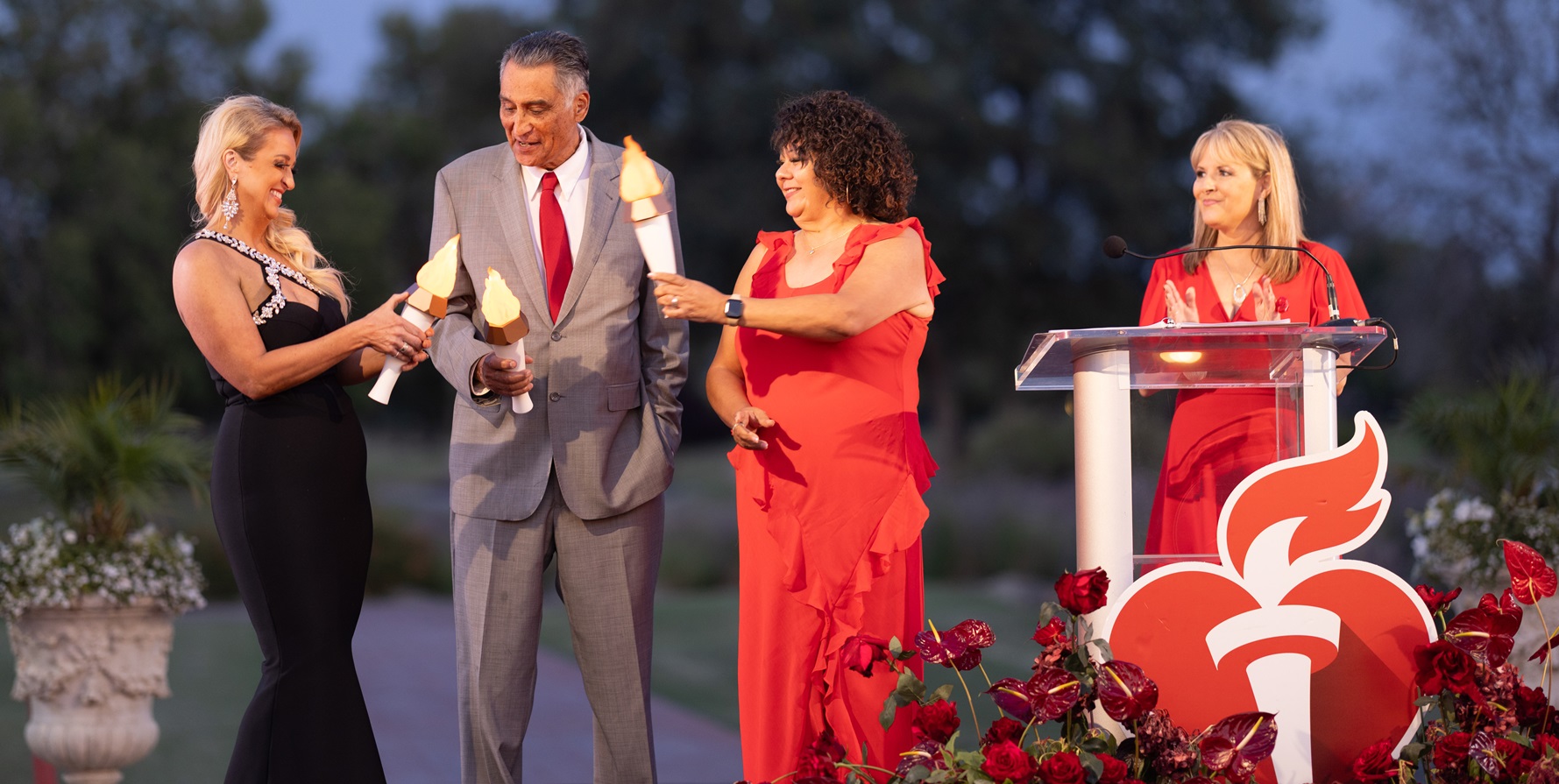 Three 2025 torch bearers on Heart Ball stage with Emcee at podium.